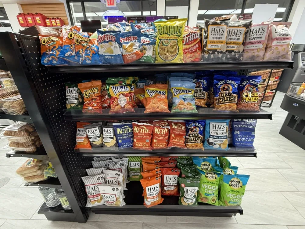 Foto ilustrativa de uma prateleira de conveniência com Ruffles, pipocas e vários salgadinhos